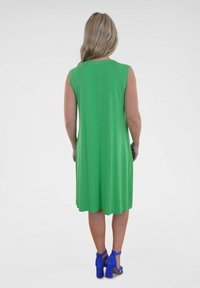 Grünes ärmelloses Kleid mit lässiger Passform, das bis zum Knie reicht. Kombiniert mit blauen High-Heel-Sandalen. Glattes, dehnbares Material.