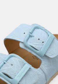 Sandale bleu clair avec un matériau texturé, deux brides réglables avec boucles bleues et une semelle intérieure marron.