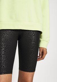 Zwarte biker shorts met een subtiele luipaardprint, van hoog-elastische stof, gecombineerd met een lichtgroen sweatshirt met een relaxte pasvorm.