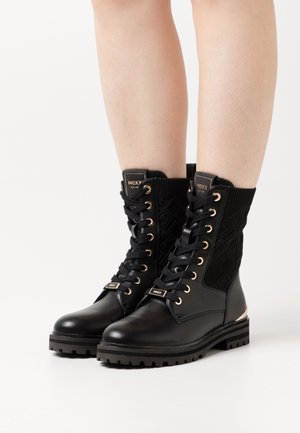 Black leather ankle boots with knitted upper, textured pattern, gold hardware accents, and sturdy rubber sole. Lace-up design with logo tag.