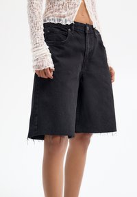 Pantalones cortos de mezclilla negra con un corte relajado, que cuentan con un dobladillo deshilachado, presillas para el cinturón, bolsillos frontales y un diseño clásico de cinco bolsillos.