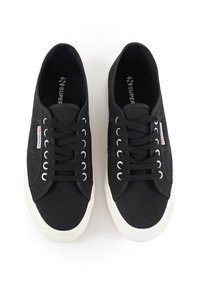 Svart canvas sneakers med hvite gummisåler, med snøring, rund tå og sømdetaljer. Logo vist på siden.