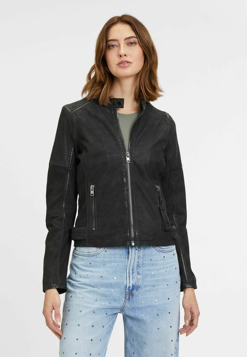 Schwarze Lederjacke mit Reißverschluss vorne, Stehkragen, vier Reißverschlusstaschen und strukturierten Schulterakzenten. Tragen über einem grünen Oberteil.