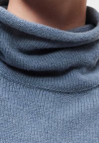 Gros plan d'une personne portant un pull à col roulé tricoté bleu doux et plié autour du cou.