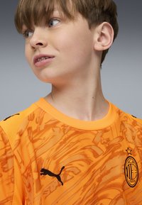 Maglia sportiva arancione brillante con motivo testurizzato, caratterizzata dal logo Puma nero e dall'emblema del AC Milan. Collo rotondo con cuciture rinforzate.