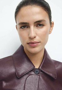 Burgundowa kurtka skórzana z dużym kołnierzem, pojedynczym zapięciem na guzik i fakturowanym wykończeniem podkreślającym jej elegancki design.