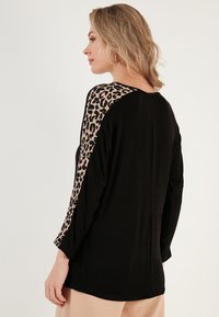 Black top featuring long sleeves in leopard print on the shoulders. Soft fabric, relaxed fit, and a round neckline.