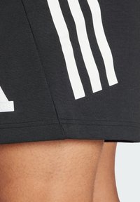 Pantaloni sportivi neri con tre strisce verticali bianche sui lati, texture liscia e logo ricamato sull'orlo inferiore.