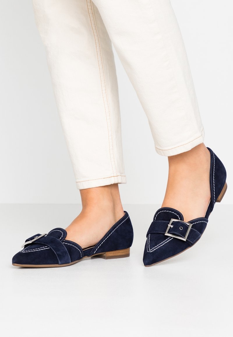Marine suède ballerina's met spitse neuzen, decoratieve gesp en witte contrasterende stiksels. Lage houten hak en slanke silhouette.