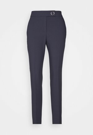 Marineblaue, schmal geschnittene High-Waist-Hose mit Frontnaht-Detail und Metallring-Schnalle am Bund, keine sichtbaren Taschen oder Verschlüsse.