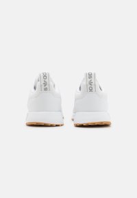 Zapatillas blancas con una parte superior de piel sintética suave, suela de goma y tiradores grises con marca. Diseño simple y moderno.