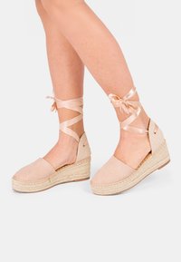 Beige espadrila kedi ar topli ar teksturētu audumu un pītu jutu zoli, ar mīksta satīna lentes potītes saitēm, nodrošinot drošu fit.