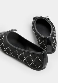 Bailarinas de ante negro con una puntera brillante negra, adornadas con patrones de diamantes con tachuelas y un lazo en la parte frontal.