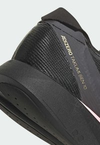 Gros plan sur le talon d'une chaussure de course noire Adidas Adizero Takumi Sen 10 avec une tige texturée et une semelle épaisse coussinée.