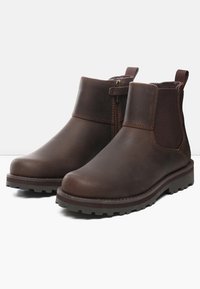 Botas de tobillo de cuero marrón con un acabado suave, paneles laterales elásticos y una suela resistente para mayor tracción. Detalle de cremallera en el lado exterior.
