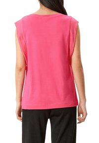 Růžový top bez rukávů vyrobený z lehkého materiálu, s kulatým výstřihem a uvolněným střihem, se subtilními švy podél okrajů.