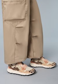 Sneakers with a beige and brown animal print, featuring mesh and leather panels, pink laces, and a textured white sole with black speckles.
