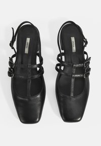 Chaussures noires en cuir avec arrière ouvert, à bouts carrés, comportant plusieurs brides et des accents de boucles sur les côtés. Texture lisse, design minimaliste.