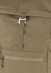 Khaki ryggsekk med glatt stoff, solid webbingstropp, metallspenne og en glidelåslomme foran med teksturert glidelåsdrag.