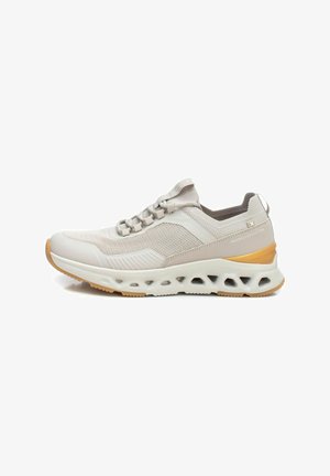 Zapatilla deportiva de color beige claro con parte superior de malla texturizada, cordones elásticos, suela acolchada y suela exterior de goma marrón con recortes.