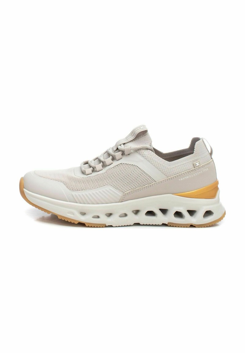 Zapatilla deportiva de color beige claro con parte superior de malla texturizada, cordones elásticos, suela acolchada y suela exterior de goma marrón con recortes.
