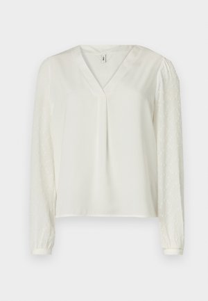 Top alb cu decolteu în V, având un material frontal neted și mâneci lungi dintr-un material transparent cu model texturat. Manșetele elastice la capetele mânecilor.