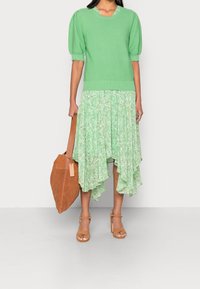 Světle zelený pulovr s nabíranými rukávy, kombinovaný s plisovanou sukní s květinovým vzorem. Hnědá semišová kabelka přes rameno a béžové lodičky.