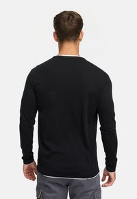 Sort langærmet skjorte med rund hals, med hvide manchetter og hvid halskant. Fremstillet af et blødt, glat stof.