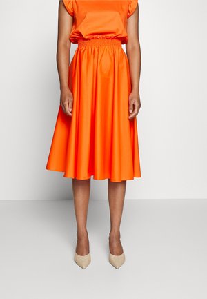 Haut orange en coton à col rond avec taille élastique, associé à une jupe orange évasée. Tissu texturé et lisse. Escarpins beiges à talons pointus.