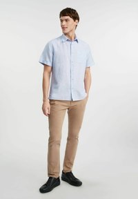 Jasnoniebieska koszula z krótkim rękawem z kieszonką na piersi, w połączeniu z beżowymi dopasowanymi spodniami i czarnymi trampkami. Gładka tekstura i swobodny fason.