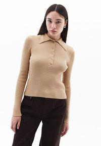 Beige ribattu neulepaita, jossa on kaulusta ja nappisuljenta, pitkähihaiset hihat. Yhdistetty tummanruskeisiin housuihin.