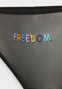 Svart nätbikini med "FREEDOM" broderat i flerfärgade trådar. Har elastiska kanter och en slät, subtil textur.