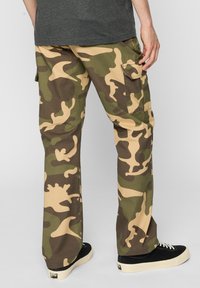 Cargo-bukser med et kamuflasjemønster i grønne og beige nyanser, med sidelommer, rett bukseben og bomullstekstur.