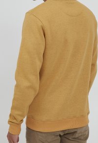 Żółta bluza z miękkiego, teksturowanego materiału, z prążkowanymi mankietami i dołem. Tylna część z minimalistycznym wzorem bez zdobień.