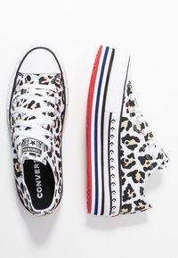 Sneakers Converse a bassa con stampa leopardata beige e nera, lacci bianchi e strisce sulla suola nei colori rosso, blu, nero e bianco.
