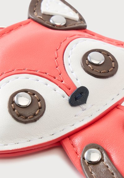 Gros plan d'un visage de renard en cuir rouge et blanc avec des yeux en rivets métalliques et des détails cousus sur un petit accessoire ou une pochette.
