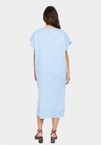 Abito lungo fino al ginocchio di colore azzurro chiaro, con una vestibilità ampia, maniche corte e spacchi laterali. Materiale morbido, design minimalista, senza motivi o dettagli.