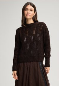 Brązowy sweter pleciony z grubą fakturą. Posiada ażurowe wzory, okrągły dekolt oraz ściągacze na mankietach i u dołu.