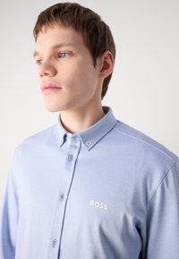 Lichtblauw overhemd met knopen gemaakt van een gestructureerde stof, met een omgeslagen kraag en een klein wit 'BOSS'-logo op de borst.