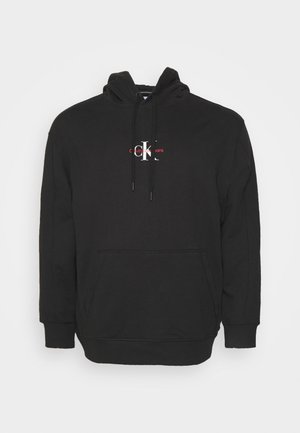 Czarna bluza z kapturem z przednią kieszenią kangurką oraz małym logo Calvin Klein Jeans w kolorze białym i czerwonym umieszczonym na środku klatki piersiowej.