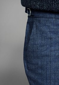 Sötétkék, texturált nadrág, finom kockás mintával. Övcsat és testre szabott szabás jellemzi. Az anyag könnyűnek és simának tűnik.