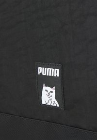Czarna torba materiałowa z prostokątną naszywką ozdobioną ilustracją kota oraz logo Puma w wyraźnym białym napisie.