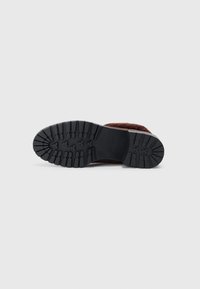 Pantof brown cu un superior texturat, asemănător cu blana. Sohletul din cauciuc negru are un model adânc pentru aderență. Design minimalist și formă.