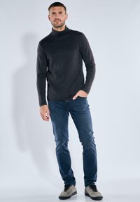 Schwarzer Rollkragenpullover mit langen Ärmeln, kombiniert mit dunkelblauen Jeans und hellgrauen Sneakers mit schwarzen Schnürsenkeln und Akzenten.