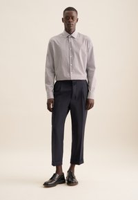 Camicia a righe con colletto, abbinata a pantaloni navy con pinces e scarpe nere stringate. Sfondo neutro.