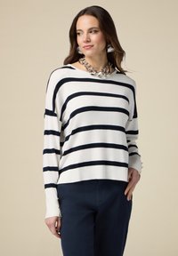 Maglione a righe in bianco e blu navy, con maniche lunghe e polsini decorati con bottoni dorati, abbinato a pantaloni blu navy scuri.