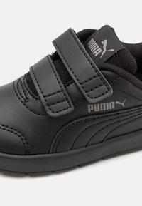 Chaussure pour enfants PUMA noire avec des bandes Velcro, tige en cuir, doublure en mesh, coutures visibles et accent logo sur le côté.