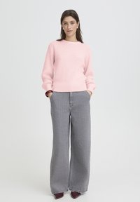 Pull rose clair texturé avec un col rond, associé à un jean gris taille haute à jambes larges et des chaussures bordeaux à bout pointu.