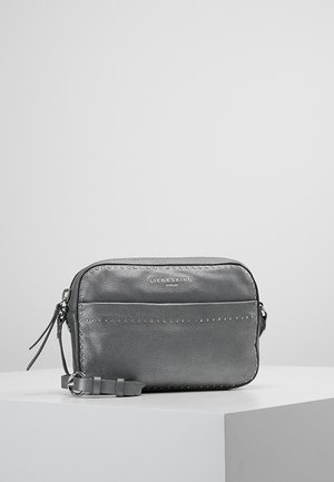 Small gray leather crossbody bag with silver studs outlining front pocket and edges, zipper closure, and adjustable strap on white surface.