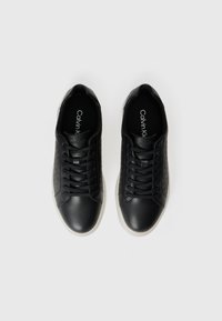 Adidași negri din piele cu secțiuni netede și texturate, având șireturi, vârf rotund și talpă din cauciuc albă. Logo-ul mărcii este vizibil în interior.